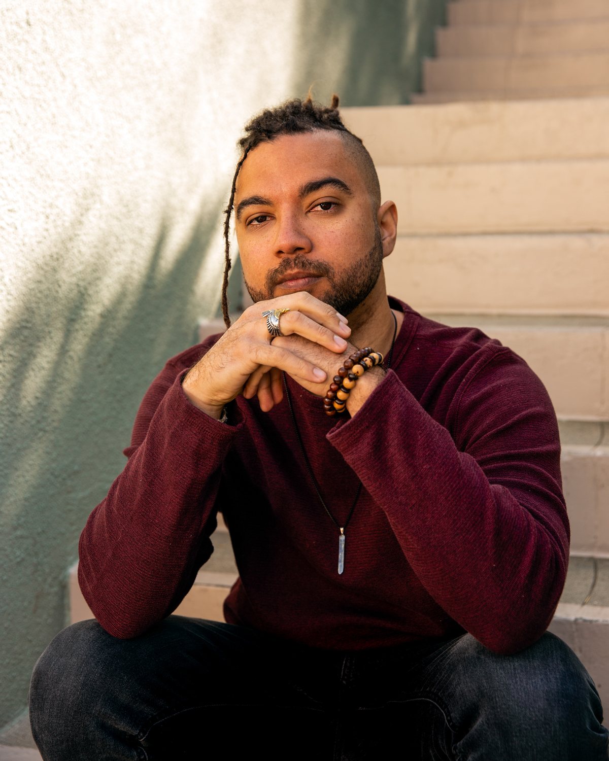Noan Ribeiro sitting on an outdoor staircase in warm afternoon light, wearing a maroon sweater, chin resting on his hands